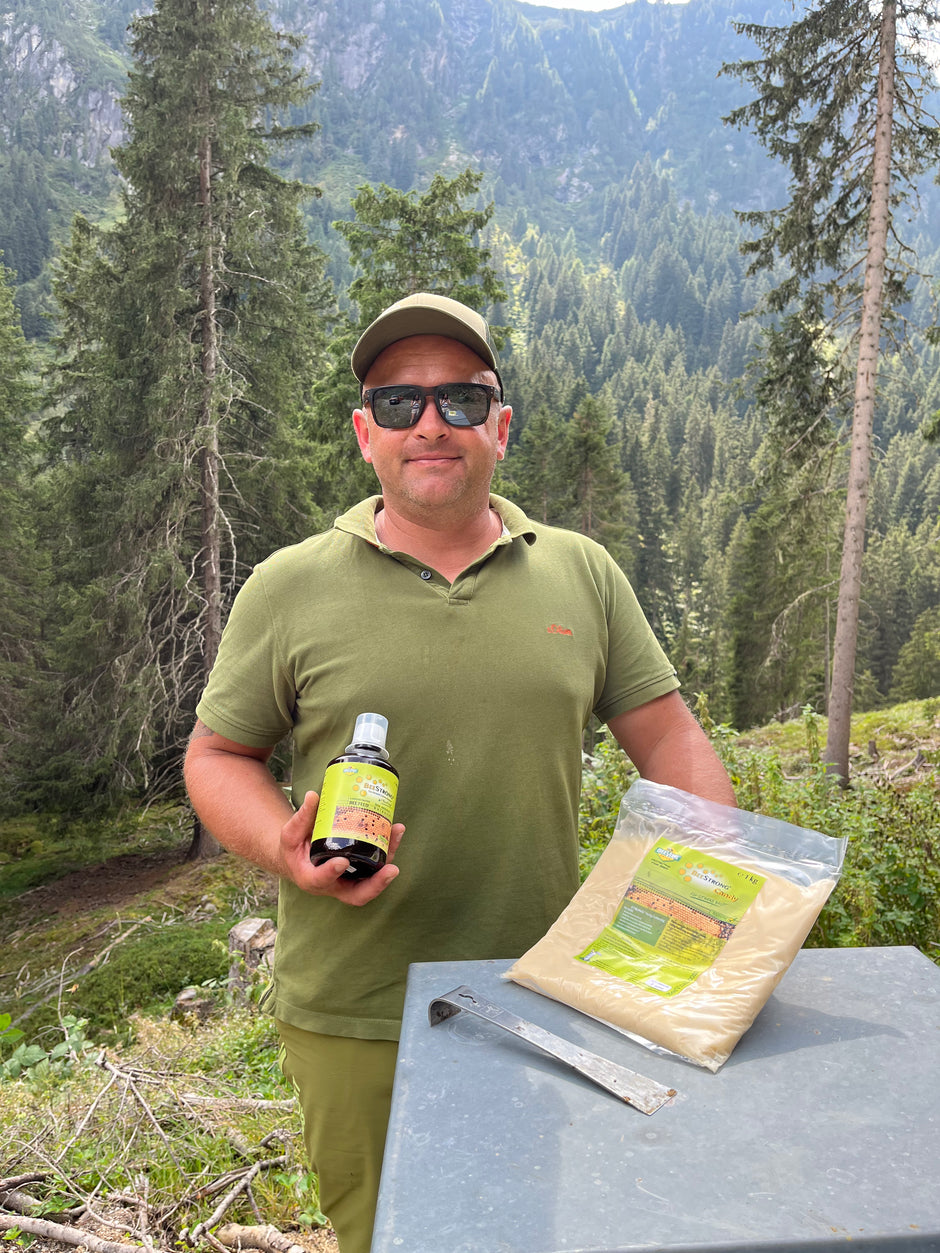 man in green t shirt holding beecandy and beestrong statnding in the mountains back to the forest