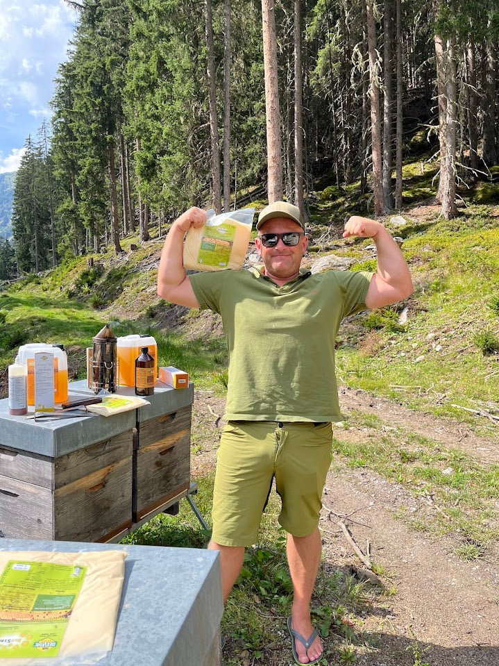 man flexing with beecandy in his hand, in the forest next to hives