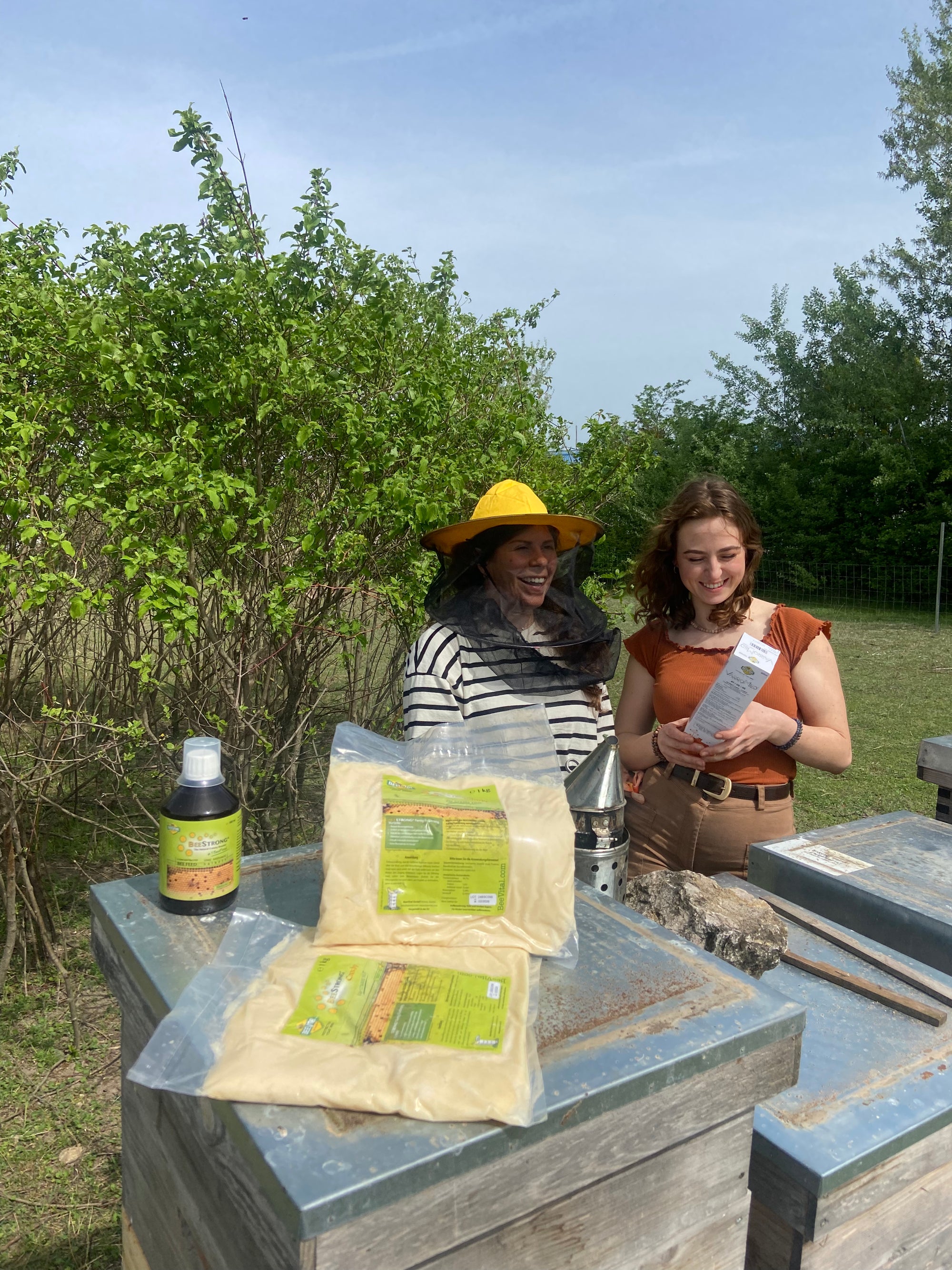 two women holding varromed with beecandy and beestrong bottles placed before them on the hives